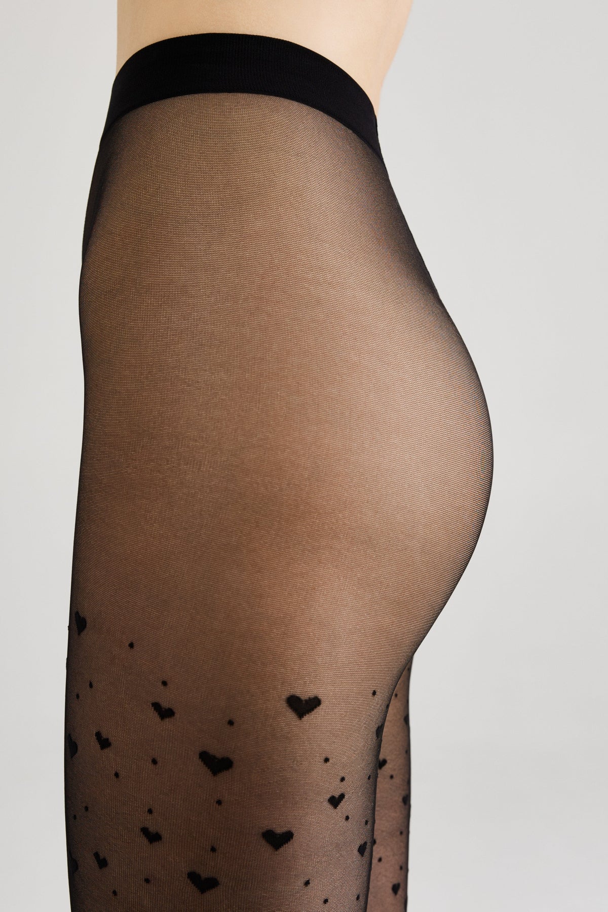 Sheer black tights featuring a pattern of small black hearts against a plain light gray background.