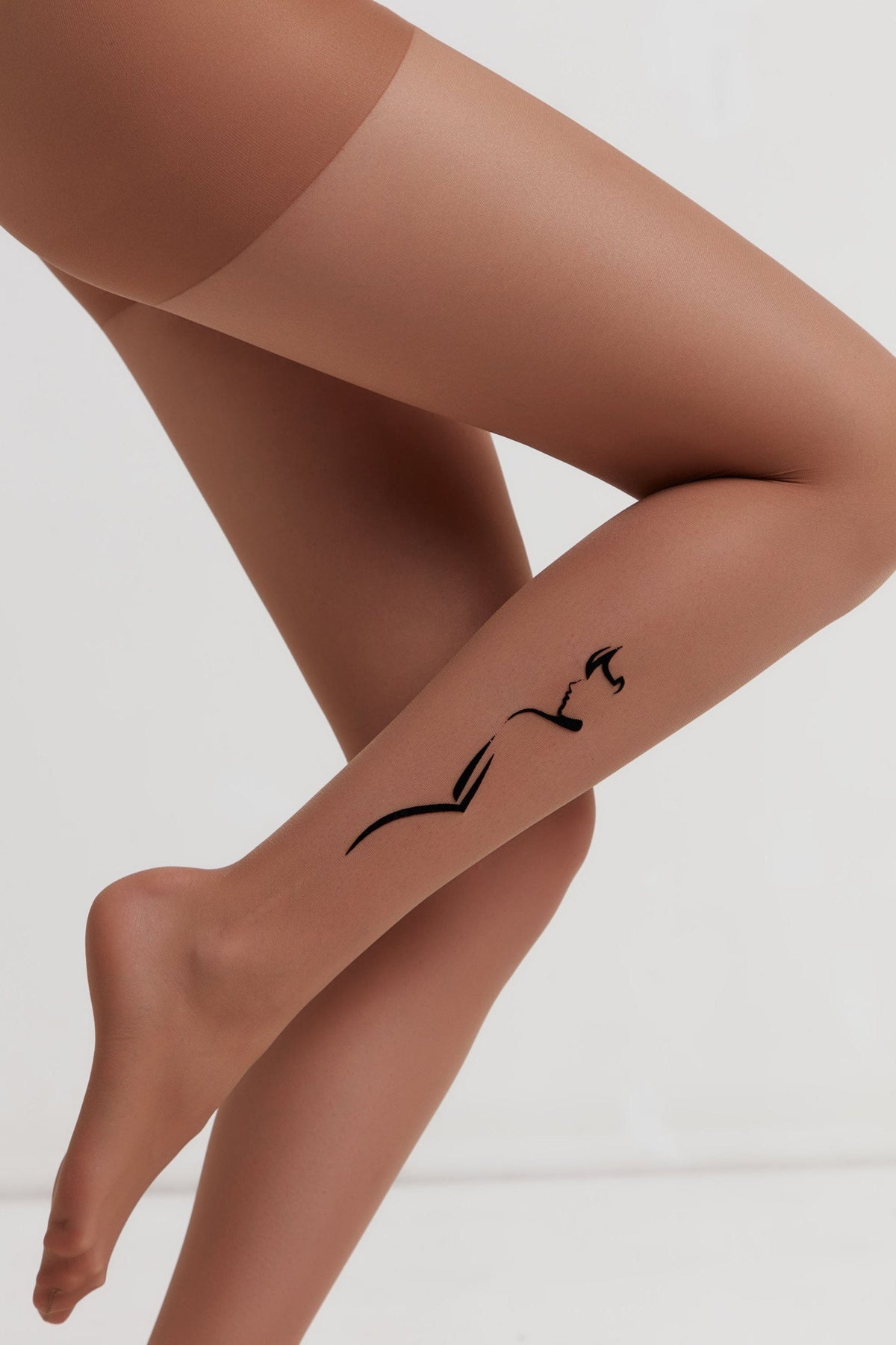 Sheer tan pantyhose worn on a person's legs, featuring a black minimalist line art drawing of a woman's profile on the side of the calf.