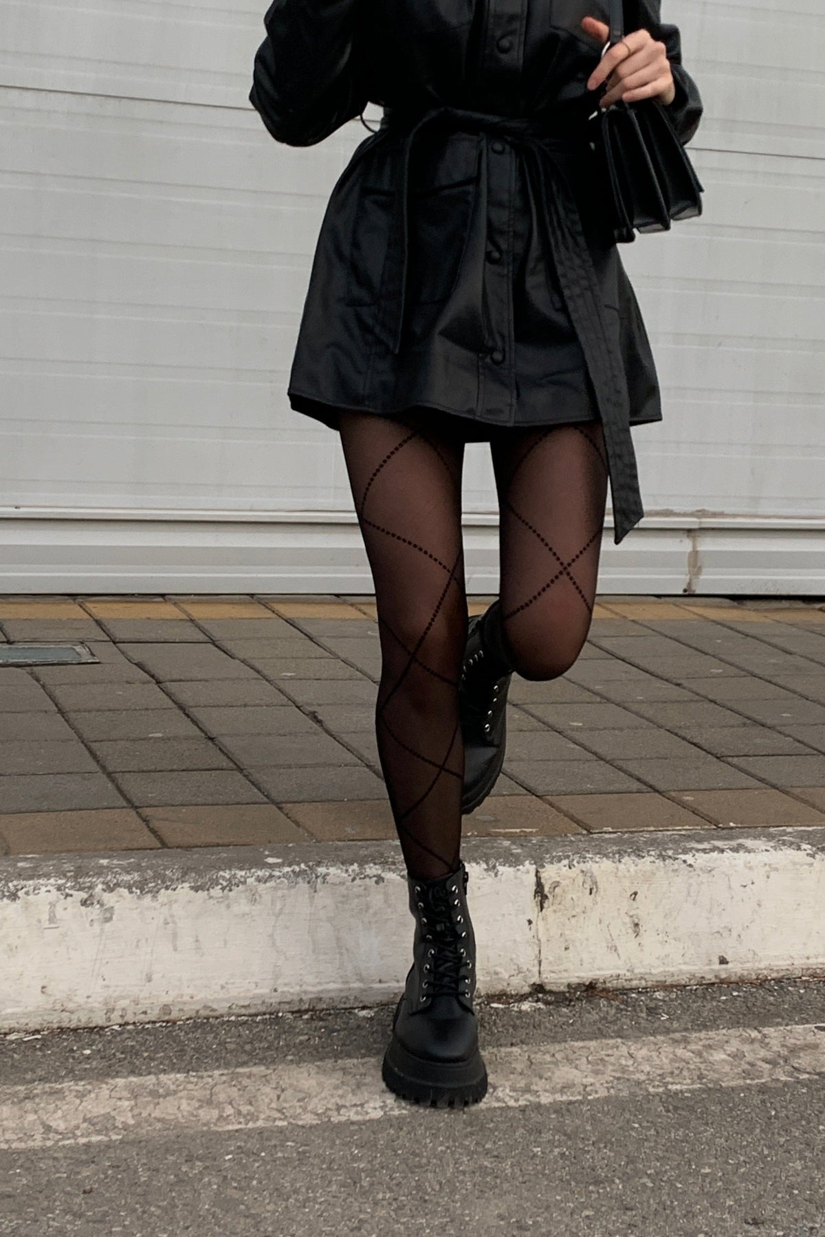 Black sheer tights featuring a diamond-shaped lattice pattern worn with a black belted mini dress and chunky black lace-up platform boots.