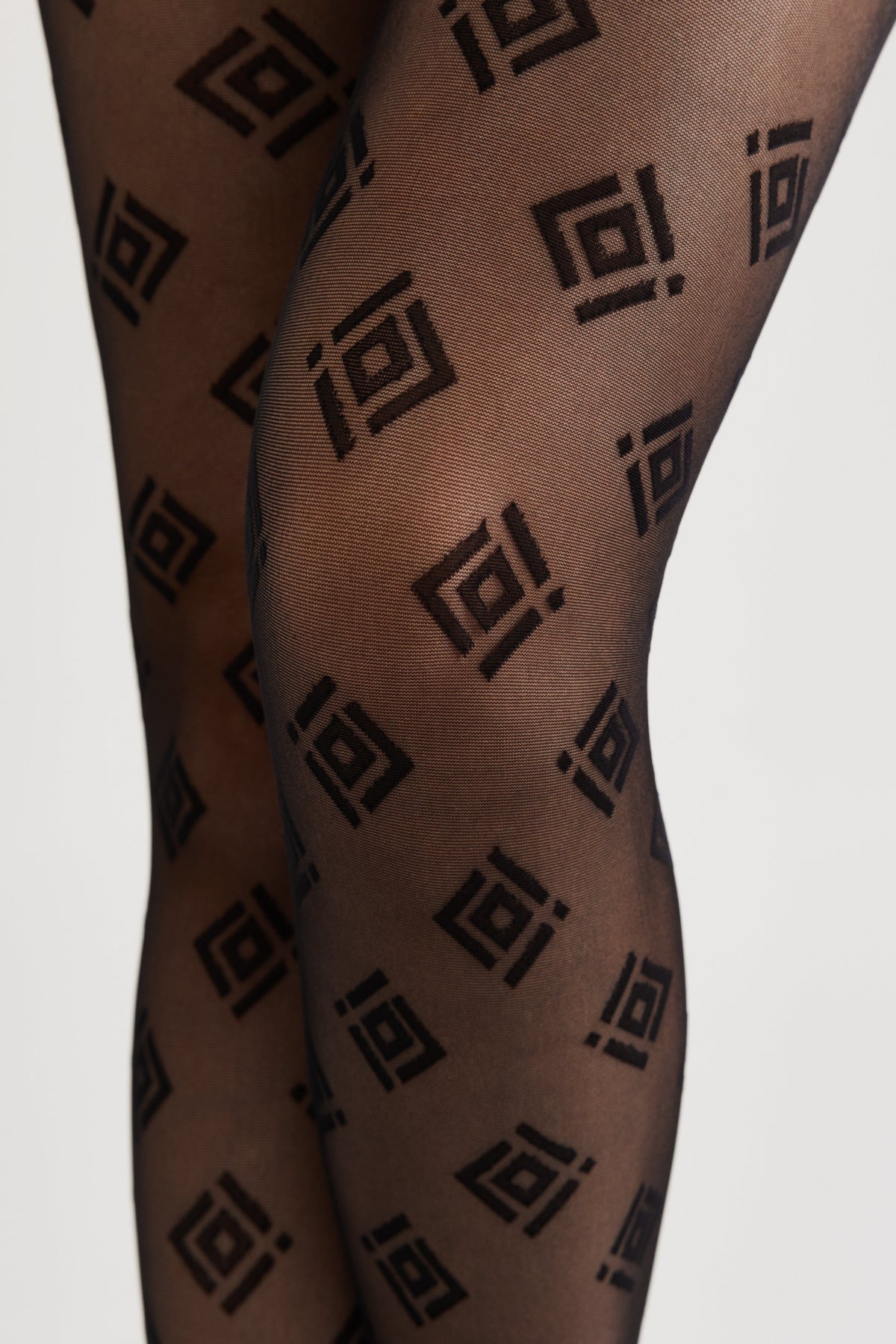 Sheer black tights feature a repeating geometric pattern of dark grey squares with a small notch on one side.