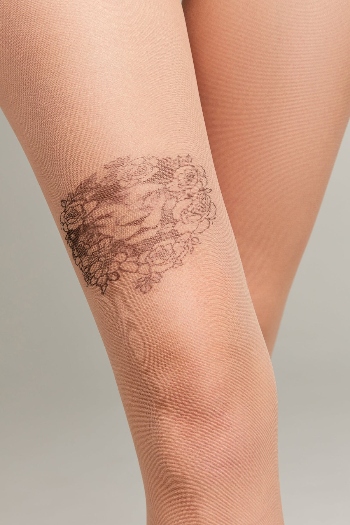 Sheer nude-colored tights feature a detailed brown printed design of a lion's head surrounded by a wreath of roses on the thigh.