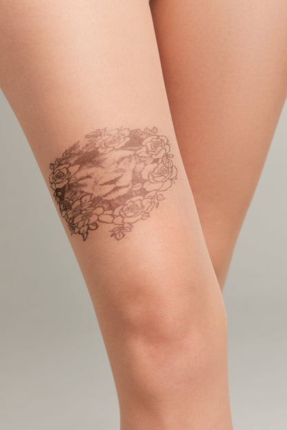 Sheer nude-colored tights feature a detailed brown printed design of a lion's head surrounded by a wreath of roses on the thigh.