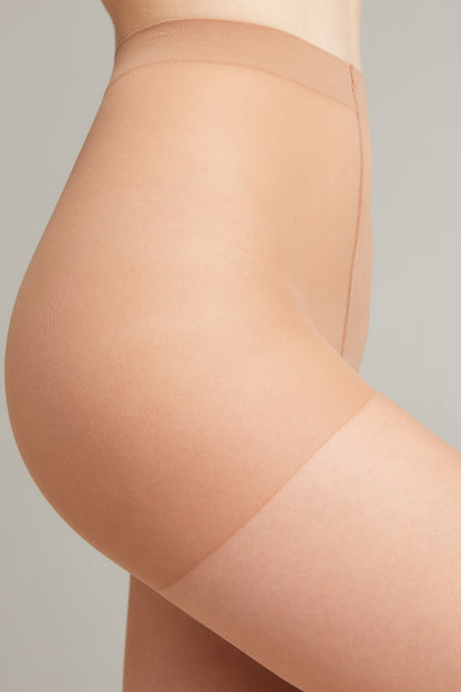 A close-up side profile of a person wearing sheer, light beige hosiery that features a reinforced waistband and upper thigh area.