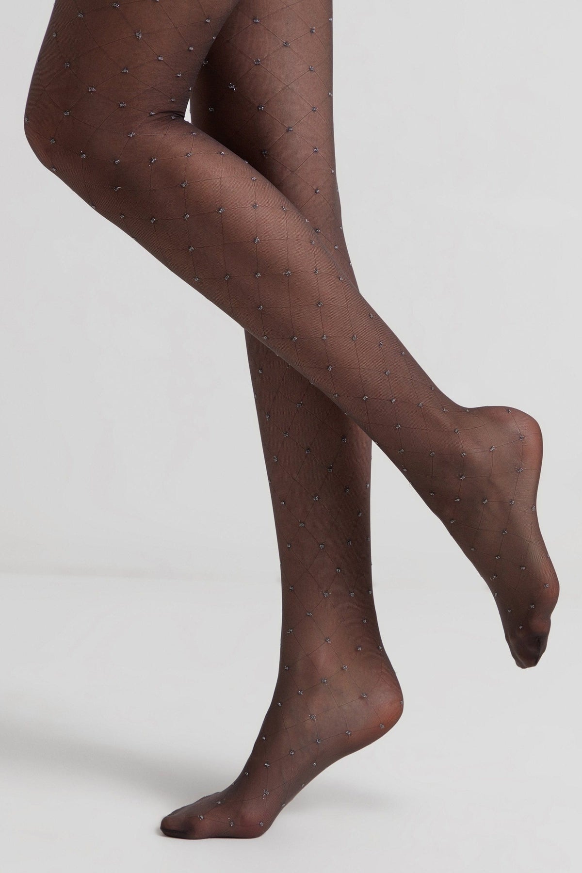Sheer black pantyhose featuring a delicate diamond-shaped grid pattern with small silver embellishments at each intersection, modeled on two crossed legs against a plain light gray background.