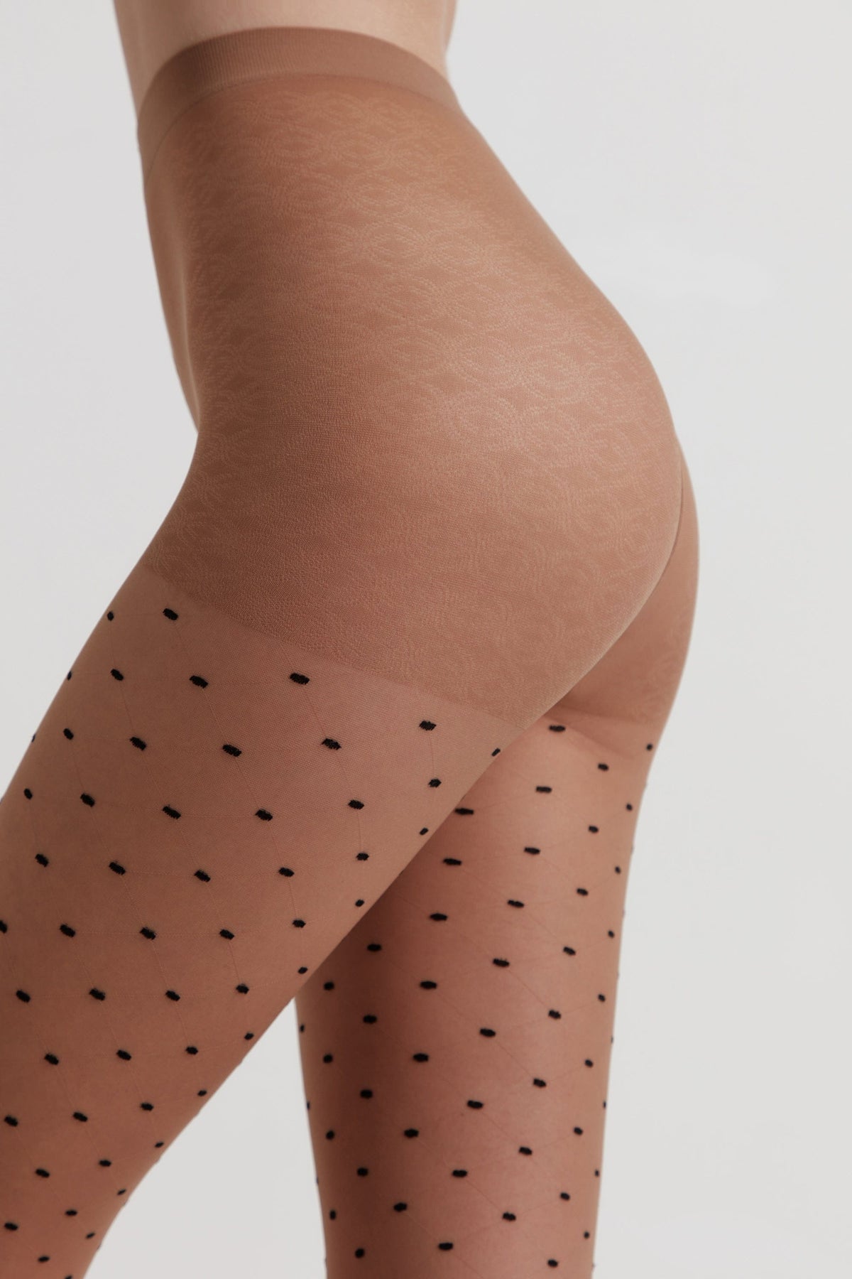 Sheer tan tights featuring a repeating pattern of small black dots on the legs and a solid reinforced panel at the upper thighs against a plain background.