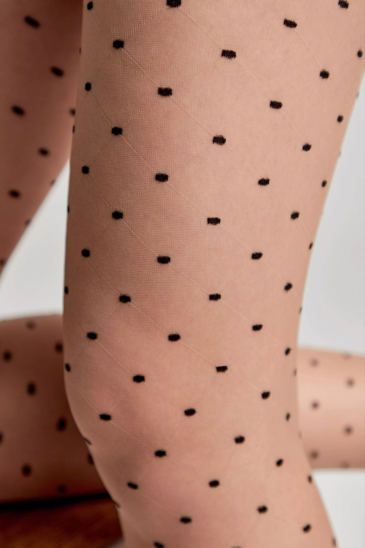 Sheer beige tights featuring a subtle diamond grid pattern with small black polka dots distributed across the fabric.