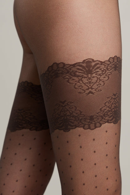 Close-up of a person wearing sheer black hosiery featuring a decorative dark brown lace garter band pattern above the knee and a subtle polka dot design on the legs.