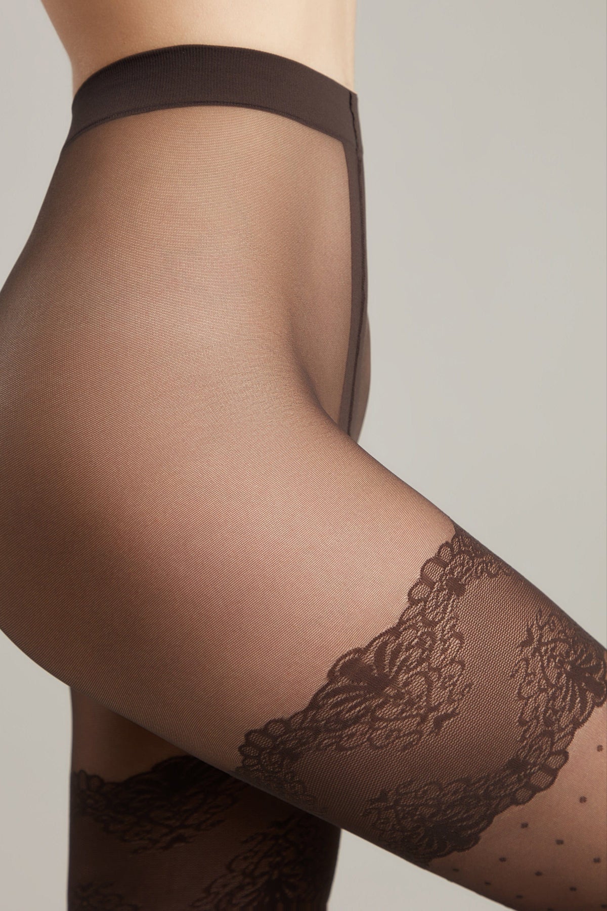 Close-up of a person wearing sheer dark brown tights featuring a decorative floral lace band around the mid-thigh.