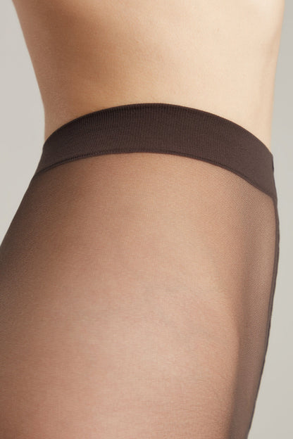 Close-up view of sheer, dark brown pantyhose worn on a person, highlighting the thick, elasticized waistband against the skin.
