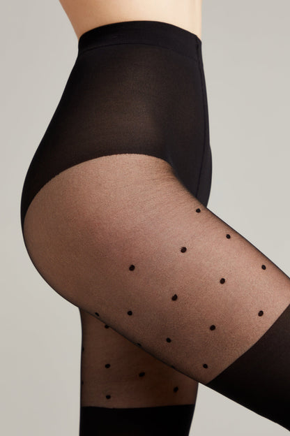 Close-up side view of a person wearing black sheer tights with a small polka dot pattern on a light grey background.