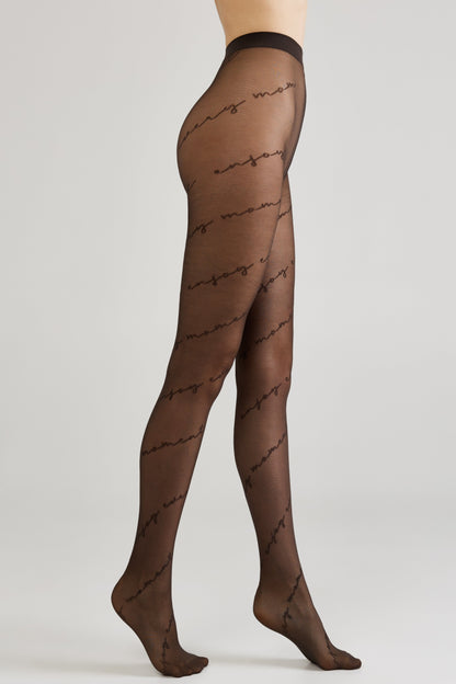 Sheer black tights worn on a person's legs, featuring a repeating cursive text pattern that reads enjoy moment.