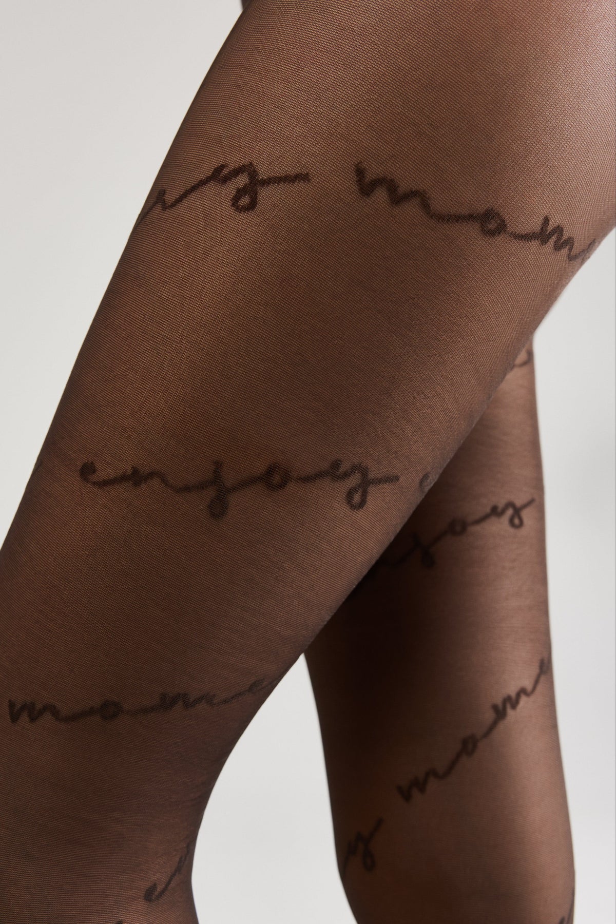 Sheer black pantyhose patterned with the repeating handwritten-style text enjoy moments in a dark brown script.