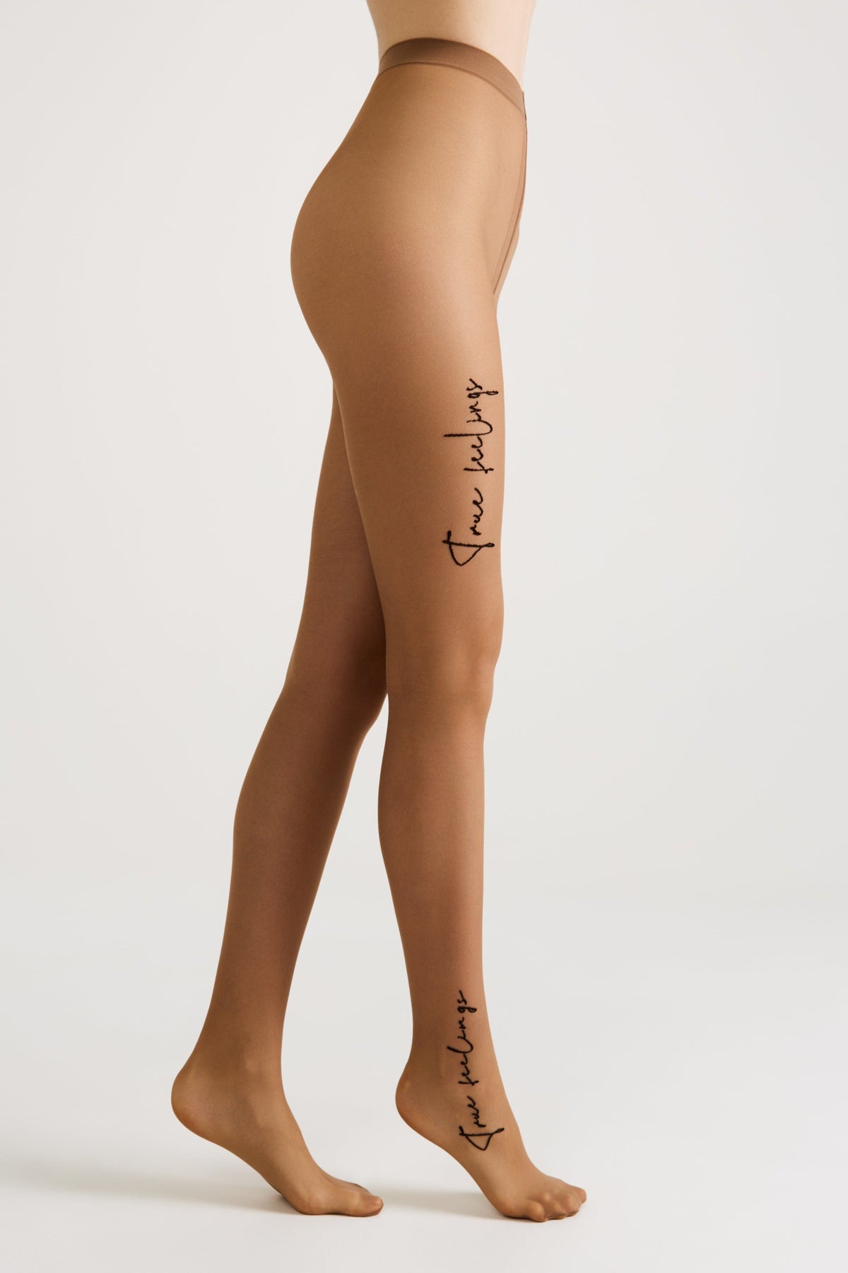 A pair of sheer tan-colored tights worn by a person, featuring the cursive words true feelings printed in black on the upper thigh and near the ankle.