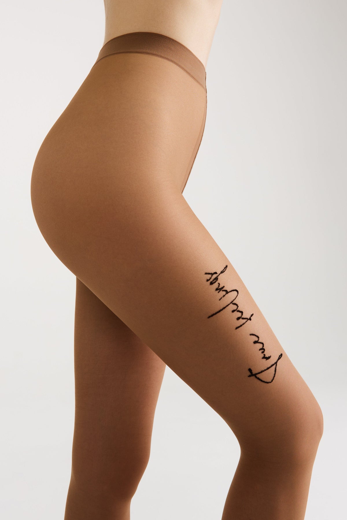 A close-up side view of a person wearing sheer tan tights with the cursive black script text true feelings printed vertically along the left thigh.