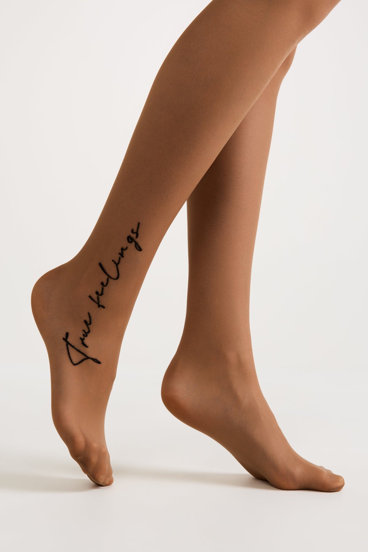 A pair of tan sheer tights features the black cursive script words True feelings printed along the side of the left lower leg.