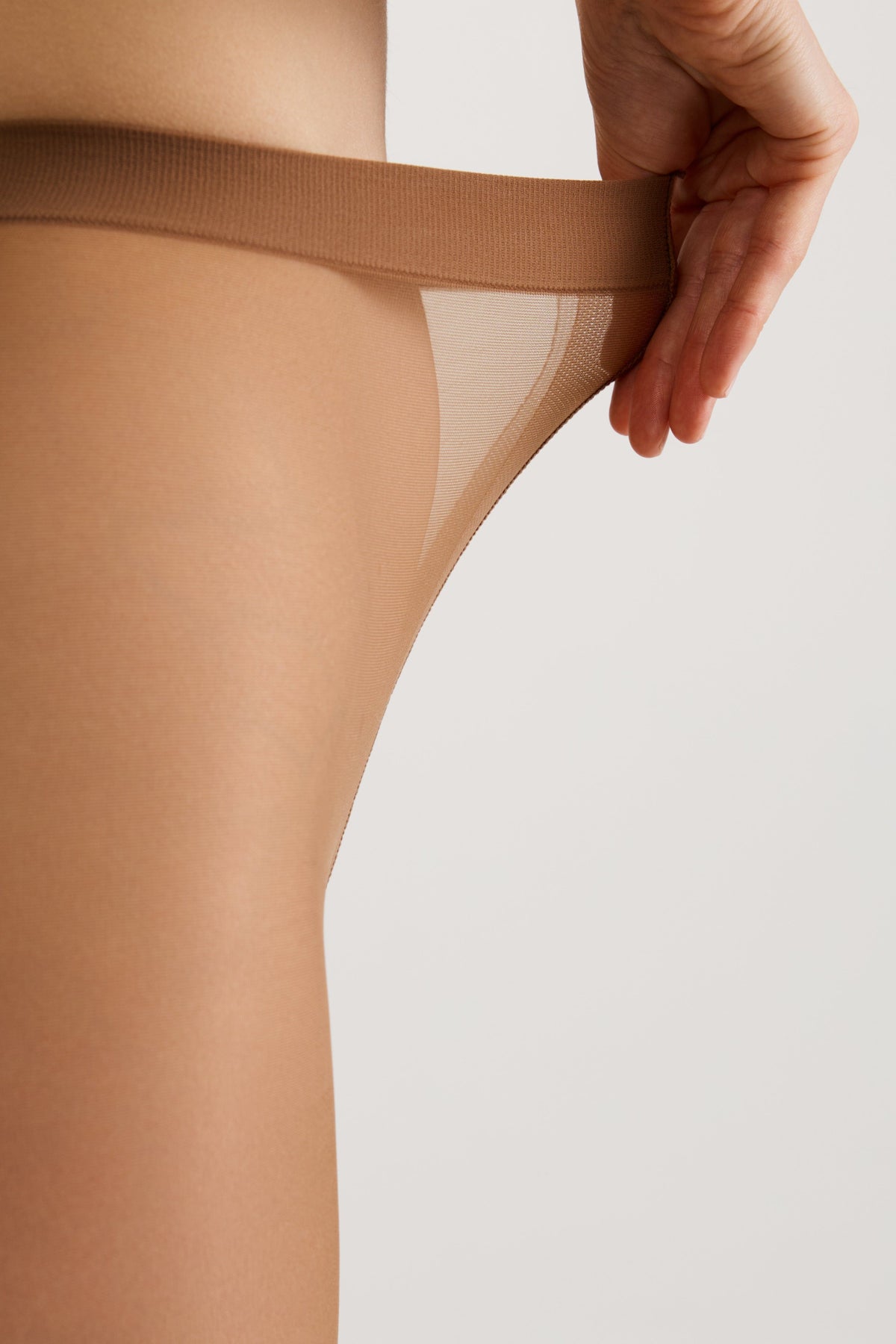 Nude-colored tights are being stretched outward by a hand against a plain white background.