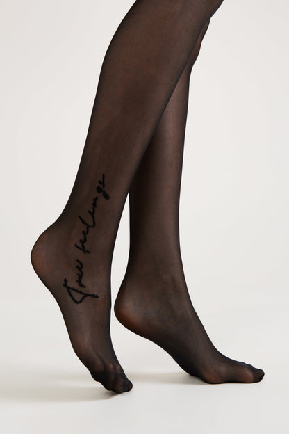 A pair of sheer black tights worn on a person's legs, featuring the cursive text "true feelings" printed on the outer side of the left ankle.