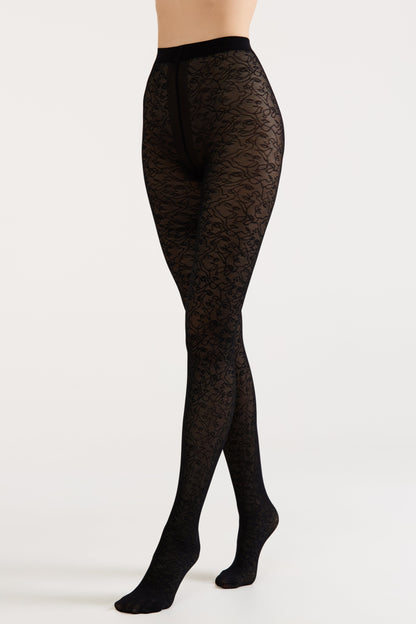 Black pantyhose with an all-over intricate abstract face pattern, shown worn on a person's legs against a plain white background.