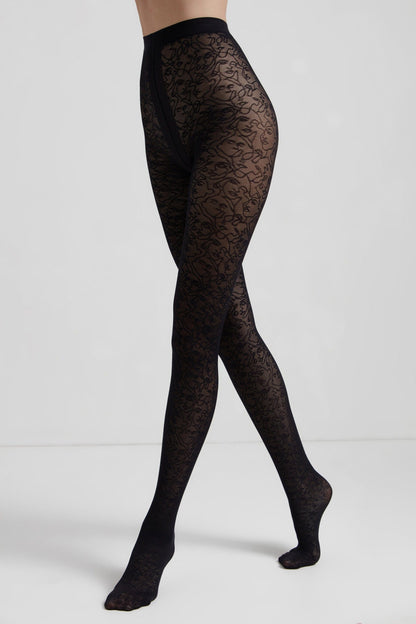 Black sheer tights with a continuous line art face pattern worn on a model's legs against a plain grey background.