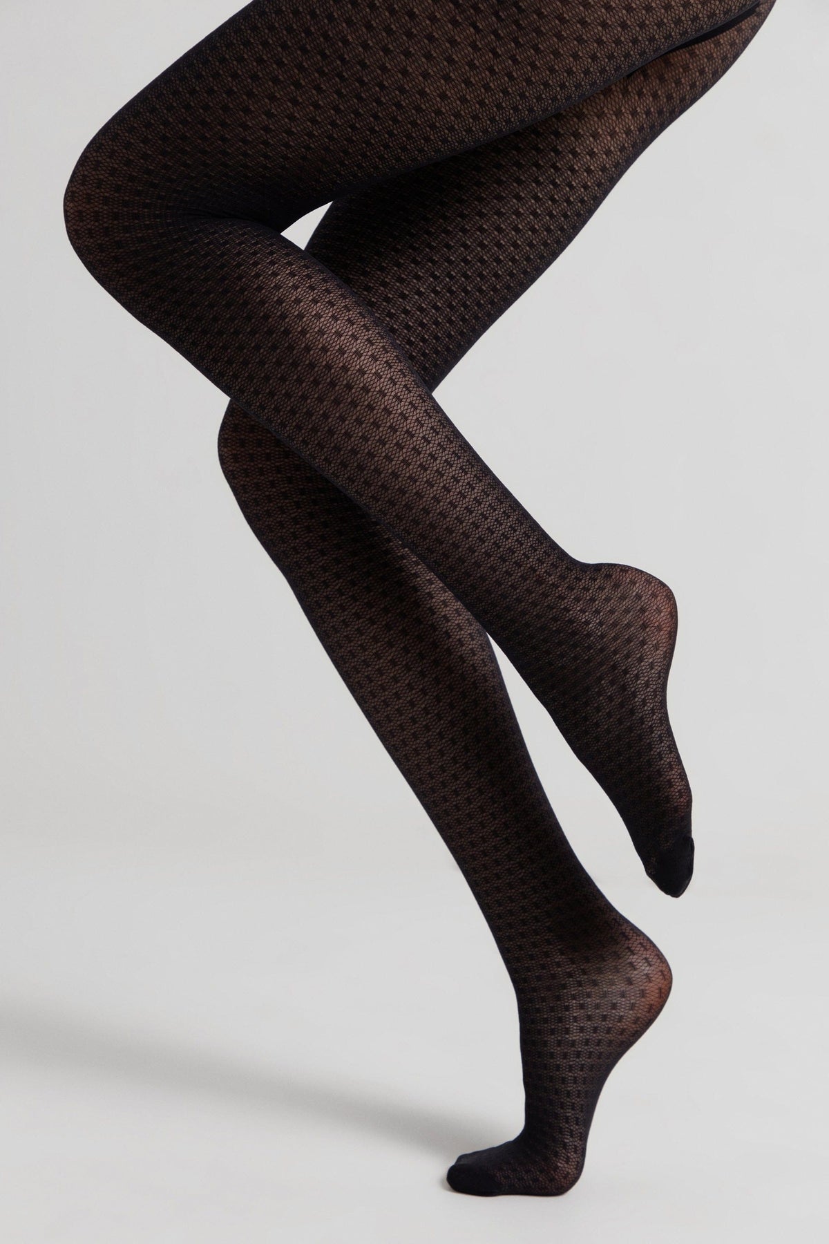 A pair of black opaque tights with a subtle textured geometric pattern worn on bent legs against a plain light gray background.
