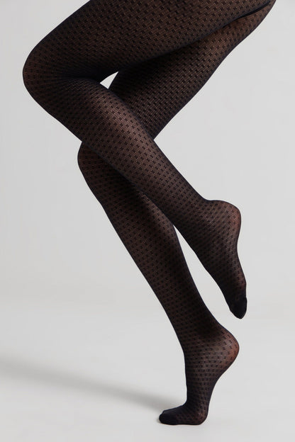 A pair of black opaque tights with a subtle textured geometric pattern worn on bent legs against a plain light gray background.
