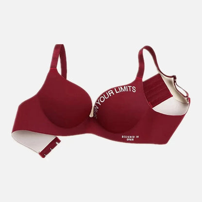 A maroon wireless bra with adjustable straps, featuring the white text SPIN YOUR LIMITS on the right cup and DESIGNED IN SPAIN on the lower band.