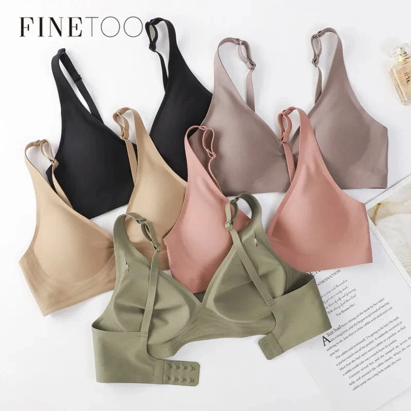 Seven seamless wireless bras in shades of black, beige, mauve, dusty pink, and olive green are arranged in a fan shape on a white surface next to a perfume bottle and a page of printed text.