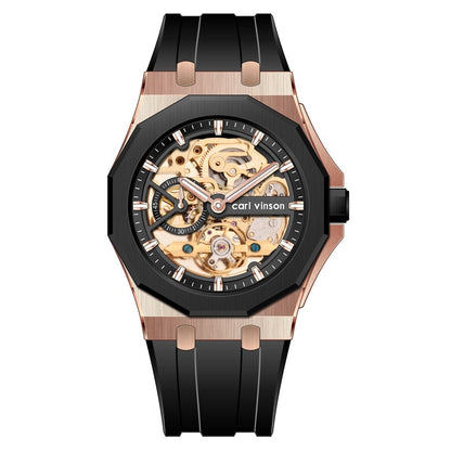 A skeleton watch with a rose gold-toned hexagonal case, a black bezel, and a black silicone strap displaying an intricate golden mechanical movement.