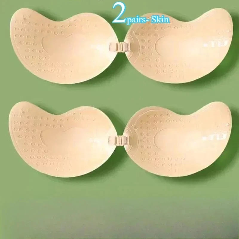 Two pairs of beige adhesive strapless bras with front clasp closures are displayed against a solid green background.