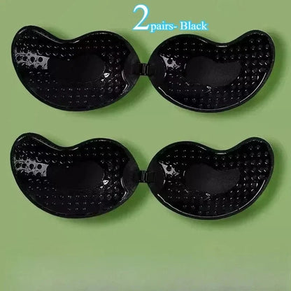 Two pairs of black adhesive bras with a curved, wing-like shape and dimpled textured surfaces arranged on a solid green background.