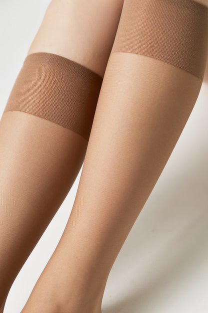 A close-up view of two legs wearing sheer, tan-colored stay-up stockings with a wide, darker beige silicone-lined band at the top.