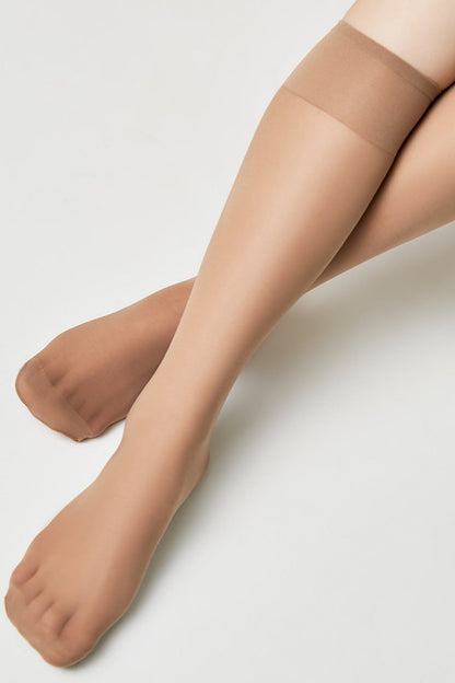 A pair of legs against a white background wearing sheer beige knee-high hosiery.