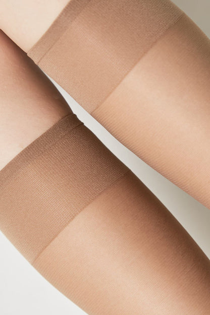 A close-up view of two legs wearing sheer nude-colored stockings with reinforced opaque bands at the top.