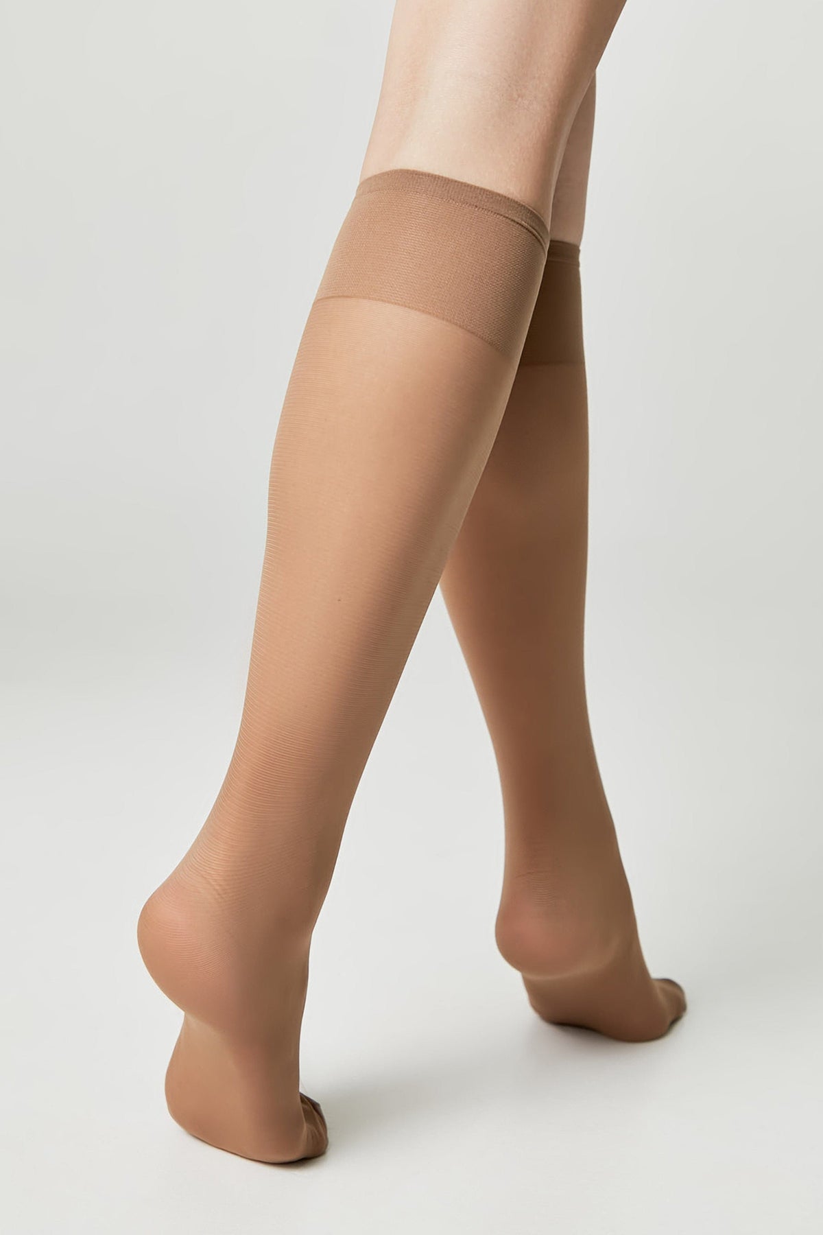 Nude-colored knee-high stockings worn on a pair of legs against a plain light gray background.