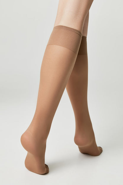 Nude-colored knee-high stockings worn on a pair of legs against a plain light gray background.