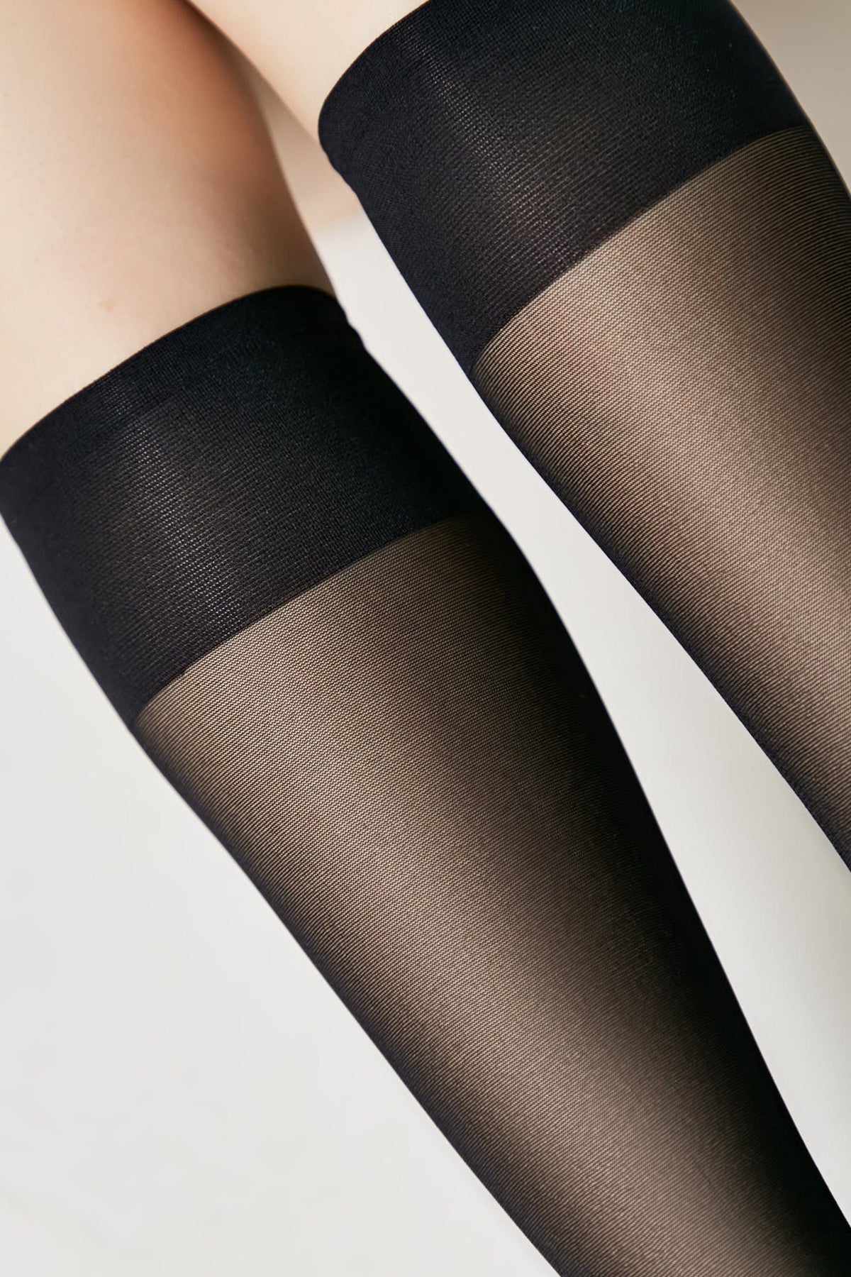 A close-up of a person wearing black sheer knee-high socks featuring a wide opaque knitted band at the top.