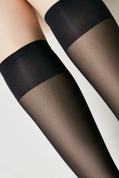 A close-up of a person wearing black sheer knee-high socks featuring a wide opaque knitted band at the top.