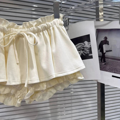 Cream-colored ruffled shorts with an elasticated drawstring waistband hanging on a display rack next to hanging photography prints.