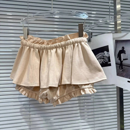 Beige tiered ruffle shorts with an elasticized waistband hanging on a clear hanger against a white slatted backdrop.