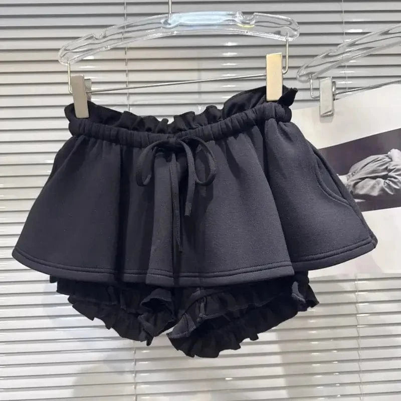 Black ruffled shorts featuring a high-waisted design with an elasticized drawstring waistband and an additional ruffled layer around the leg openings, displayed on a hanger.