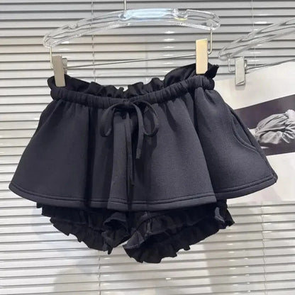 Black ruffled shorts featuring a high-waisted design with an elasticized drawstring waistband and an additional ruffled layer around the leg openings, displayed on a hanger.