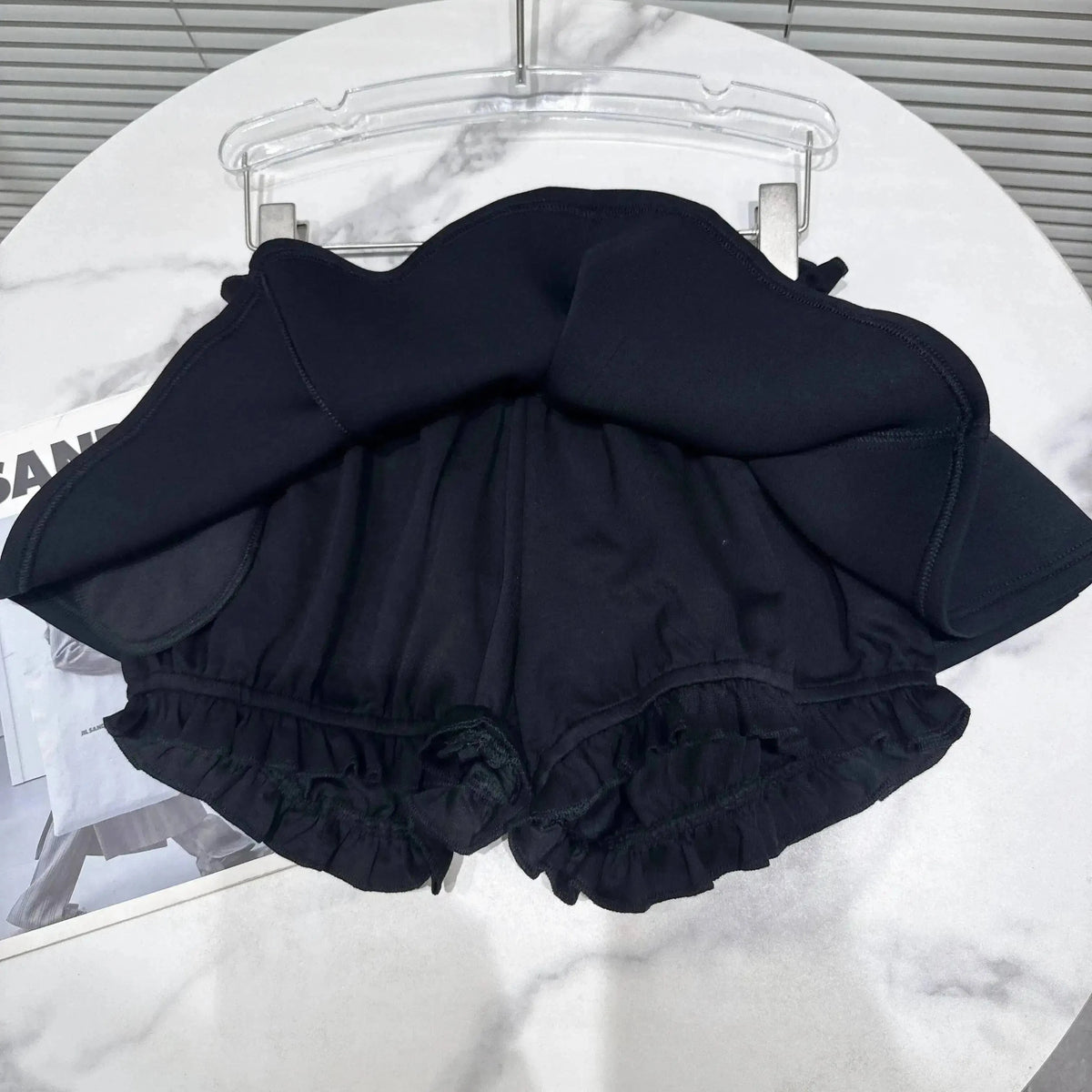 A black skort with an A-line skirt overlay and ruffled leg openings sits on a white marble table.