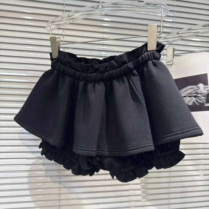 A black ruffled mini skirt with an elastic waistband hangs from a transparent hanger against a white slatted background.