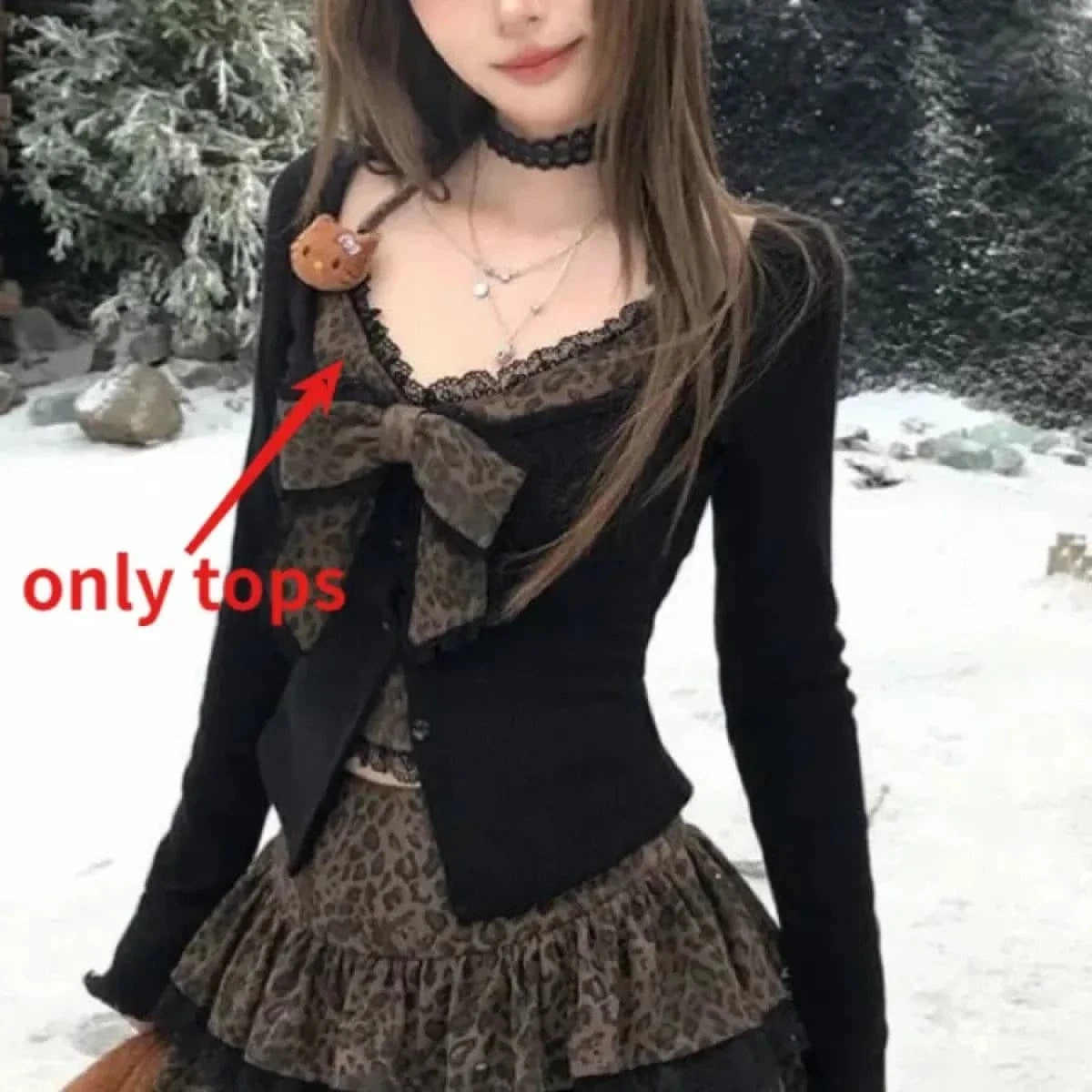 A black long-sleeved button-up cardigan worn over a brown leopard-print tank top featuring a lace trim and a large bow detail on the neckline, shown in a snowy outdoor setting.