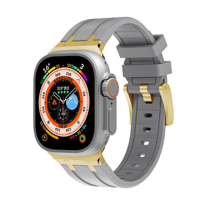 A smartwatch with a rectangular display and a colorful circular face sits attached to a gray silicone watch band featuring gold-tone metal connectors and a matching buckle.