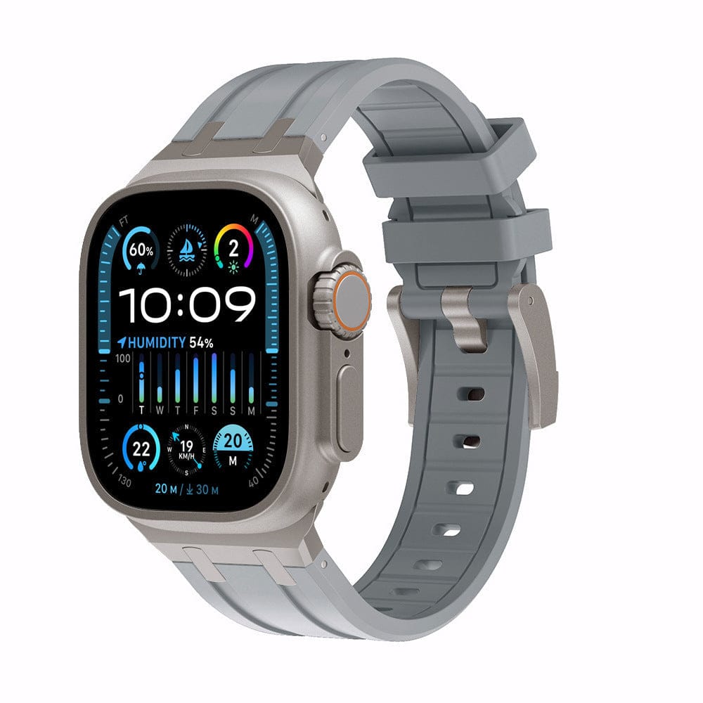 A smartwatch with a rectangular, metallic-toned casing and a light grey silicone strap sits against a plain white background, displaying a digital watch face with various weather and environmental data points.