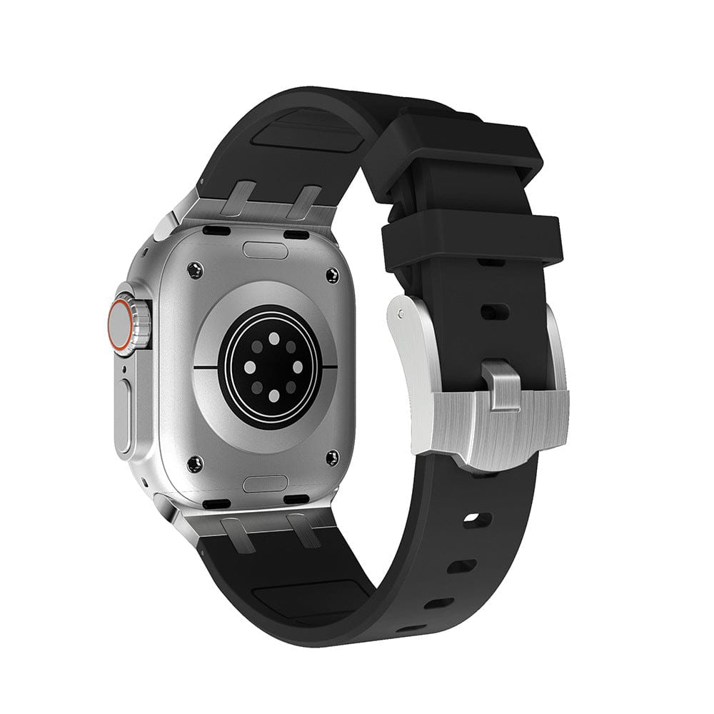 A silver-toned smartwatch with a black silicone strap is shown from a rear angle, highlighting its circular sensor array, metallic casing, and buckle fastener.