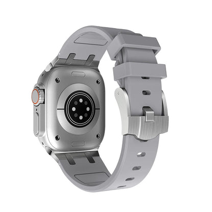 A smart watch with a silver case and a grey silicone strap viewed from the back, showing the sensor array and metal buckle.