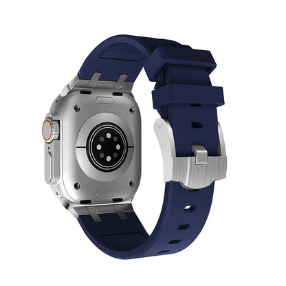 A smartwatch with a silver metallic rectangular case and a dark blue silicone band, shown from the back to reveal the circular heart rate sensor and metal buckle clasp.