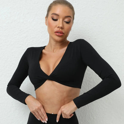 A woman wearing a black long-sleeved cropped top with a twisted detail at the center of the V-neckline against a white textured background.